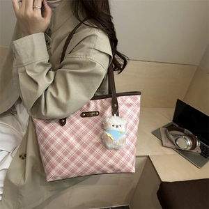 Pink plaid tote bag with brown straps and cute teddy bear charm on office desk background