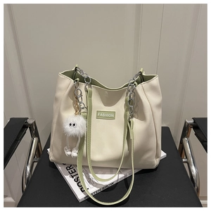 Détail du sac cabas crème avec bordure verte, étiquette fashion et breloque en peluche blanche