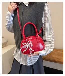 Detail of red patent leather mini bag with pearl bow and lace ribbons on a model