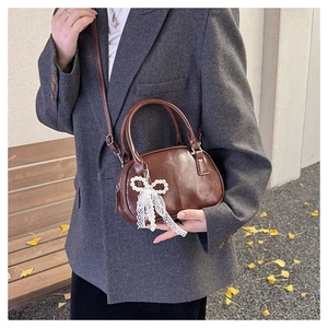 Detail of a brown leather bag with pearl bow charm on an autumn street background