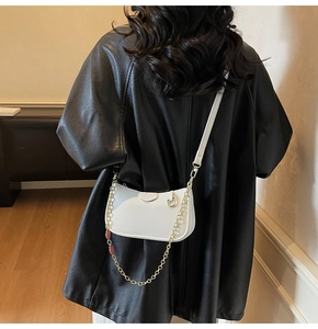 Close-up of white lychee pattern leather baguette bag with gold chain and leather strap