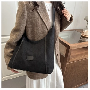 Close-up of black suede hobo bag with decorative stitching on a brown blazer outfit