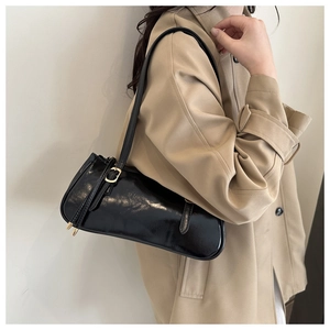 Detail of a black glossy baguette shoulder bag with gold hardware on a beige trench coat