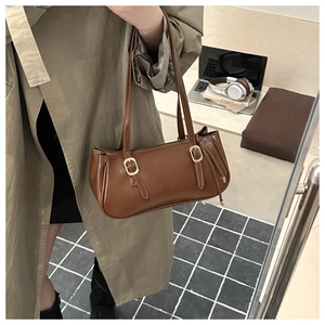 Brown vintage baguette bag with gold buckles shown on shoulder in stylish urban setting