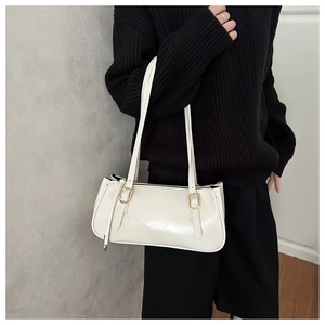 Close-up of white glossy leather shoulder bag with gold hardware worn by a model