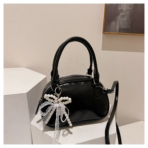 Detail of glossy black handbag with pearl bow charm and lace ribbon on display stand