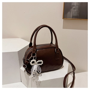Close-up of a dark brown glossy handbag with pearl bow and lace ribbon details