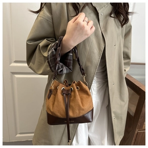 Detail of a brown suede drawstring bucket bag featuring a woven handle and leather base