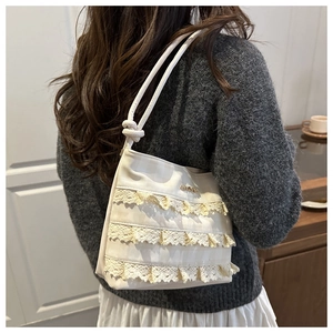 Detailed close-up of cream canvas bucket bag featuring elegant triple-layer lace trim detail