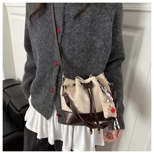 Detail of canvas bucket bag with leather trim, featuring a silk scarf and cookie charm