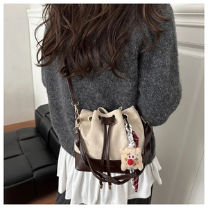Detail of a retro drawstring bucket bag with beige suede contrast and a plush pendant