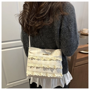 Close-up of cream lace crossbody bag with layered frills and gold logo on the strap