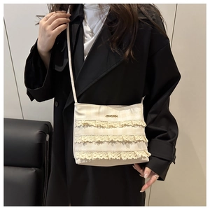 Detail of beige crossbody bag with textured fabric, lace layers and gold logo plate