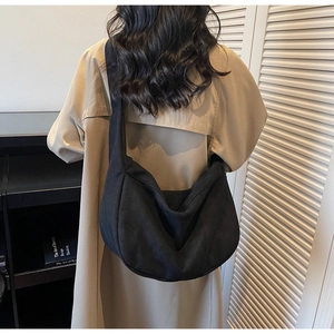 Detail shot of the large black half-moon crossbody bag on a model in a camel coat
