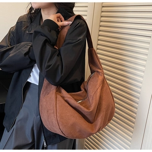 Detail of reddish brown suede tote bag featuring crescent shape and silver metal zipper
