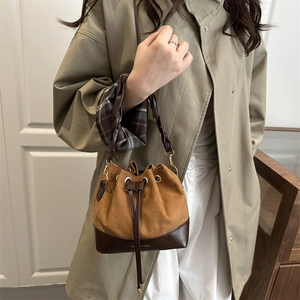 Brown suede drawstring bucket bag with woven handle shown styled with a green trench coat