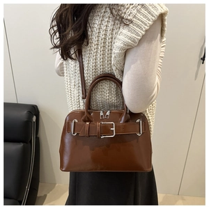 Bolso tipo concha de cuero brillante marrón con hebilla plateada usado por modelo