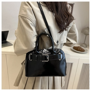 Fashionable black glossy shell bag worn over the shoulder in a modern office setting