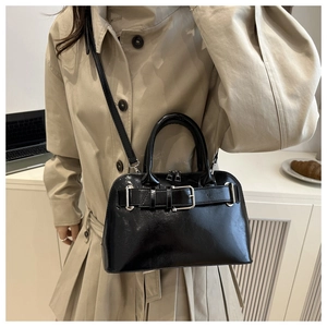 Detalle de bolso negro brillante con hebilla plateada y correa de hombro ajustable