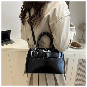 Bolso de charol negro pulido con detalle de hebilla plateada en un entorno lifestyle
