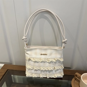 Creamy beige bucket bag with lace layers and woven straps on a glass coffee table