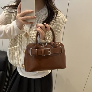 Bolso de charol marrón con hebilla mostrado en un elegante selfie de mano frente al espejo