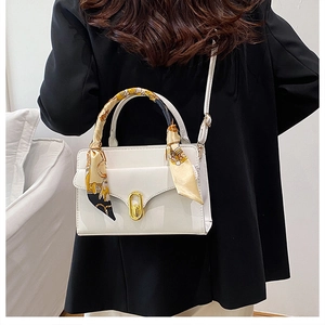 Close-up of white leather handbag with gold oval clasp and decorative floral silk scarf
