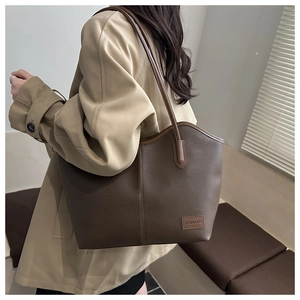 Detail of a brown large capacity tote bag with lychee grain leather and fashion label