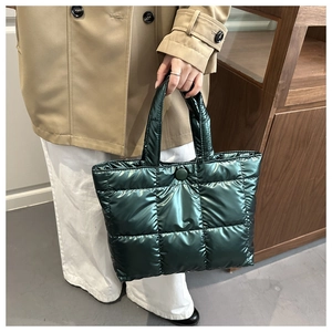 Detail of dark green quilted tote bag showing metallic gloss and puffed texture on hand