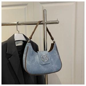Detail of blue denim shoulder bag with brown leather trim and silver metal M logo