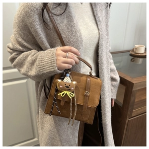Detail of a brown suede satchel with a metal buckle and a cute teddy bear pendant