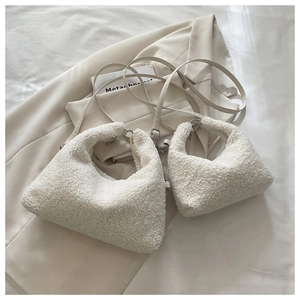 Close-up of two white faux shearling crescent bags with leather straps on a beige blazer