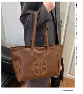 Detail of a brown leather tote bag with embossed circular logo for autumn fashion