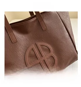 Detail shot of brown tote bag featuring wrinkled leather texture and circular cut-out AB logo