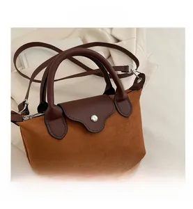 Detail of brown suede mini tote with leather flap, silver hardware, and shoulder strap
