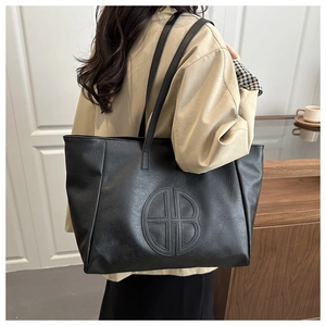 Detail of black tote bag with embossed logo and leather texture on khaki coat