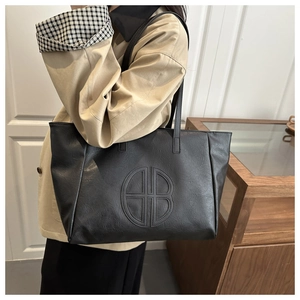Litchi texture black tote bag with embossed logo shown on shoulder in daily setting