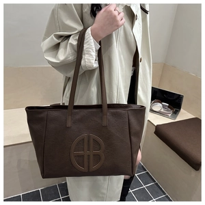 Detail of dark brown tote bag featuring oversized circular logo and fine pebbled leather texture