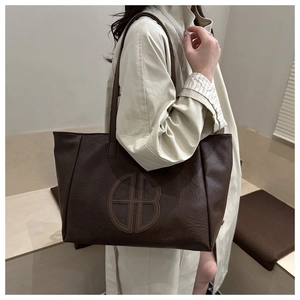 Close-up of dark brown leather tote bag showing embossed HB logo and fine grain texture