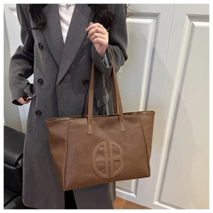 Detail of deep brown tote bag with embossed circular logo on pebbled leather surface