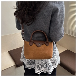 Detail of caramel suede dumpling bag with dark leather handle and silver buckle on model
