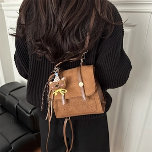 Brown retro leather backpack with bear pattern and plush charm on a black sweater