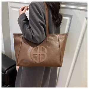 Brown oil wax leather tote bag with round logo shown on shoulder for size reference
