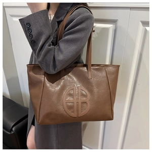 Detail of a brown tote bag in pleated PU leather featuring a circular cutout logo design