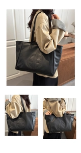 Detail view of large black tote bag featuring pebbled leather texture and circular logo