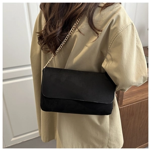 Minimalist black suede crossbody bag with gold chain strap shown on a model