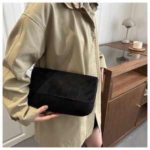 Detail shot of a black suede crossbody bag with gold chain strap on a model in a trench coat