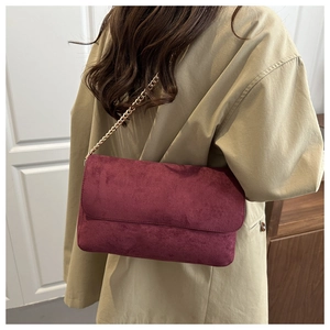 Detail of burgundy suede shoulder bag with golden chain strap on model's side
