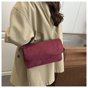 Detail of burgundy suede shoulder bag with golden chain strap on a model outfit