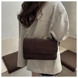 Detail of dark brown suede shoulder bag with gold chain strap on beige blazer